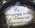 Uszkodzona porcelanowa tabliczka pamiątkowa przytwierdzona do żeliwnego krzyża
