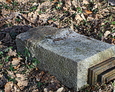 Przewrócony kamienny postument z fragmentem podstawy żeliwnego krzyża