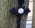 Żeliwny krzyż z nagrobka dziecięcego przytwierdzony do jednego z drzew
