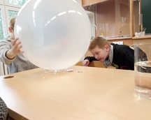 ,,Magiczny balon" - jeden z chłopców trzyma duży balon nad skrawkami papieru, drugi z chłopców dokonuje obserwacji.