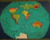 Dzieci wykonują konturową mapę świata  z wykorzystaniem barwionego ryżu. Na mapie zaznaczono wyzyny, niziny, góry  oraz morza i oceany.