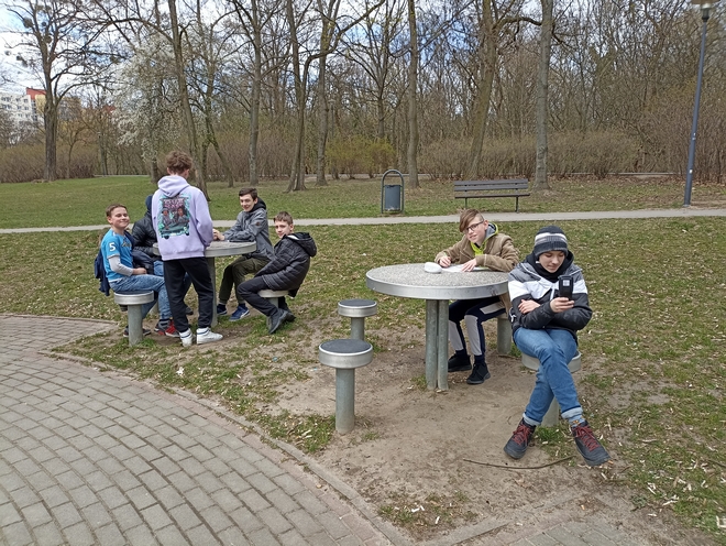 Uczniowie siedzą przy stolikach w parku i dokonują pomiaru parametrów fizykochemicznych.
