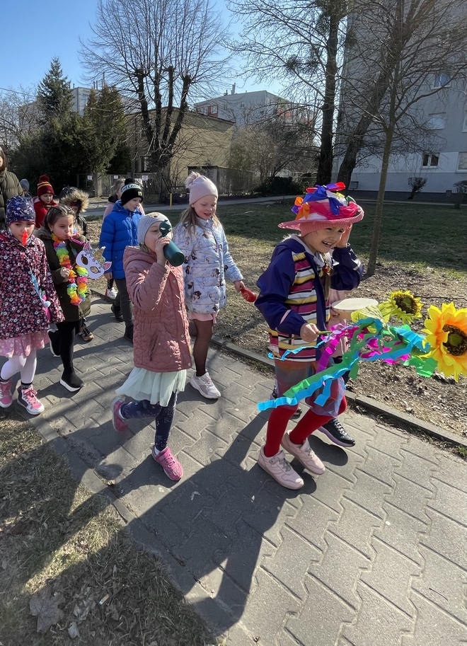 Uczniowie w kolorowych strojach spacerujący ulicami Raszyna.
