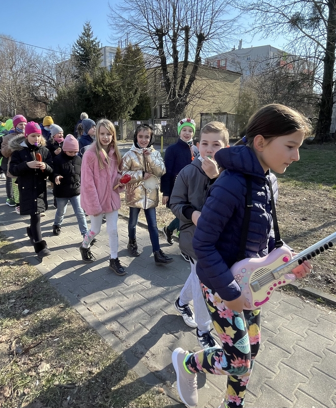 Uczniowie w kolorowych strojach spacerujący ulicami Raszyna.