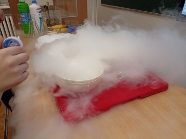 Na stole znajdują się miski z suchym lodem i wrzątkiem. Widać roznoszący się ,,dym". 