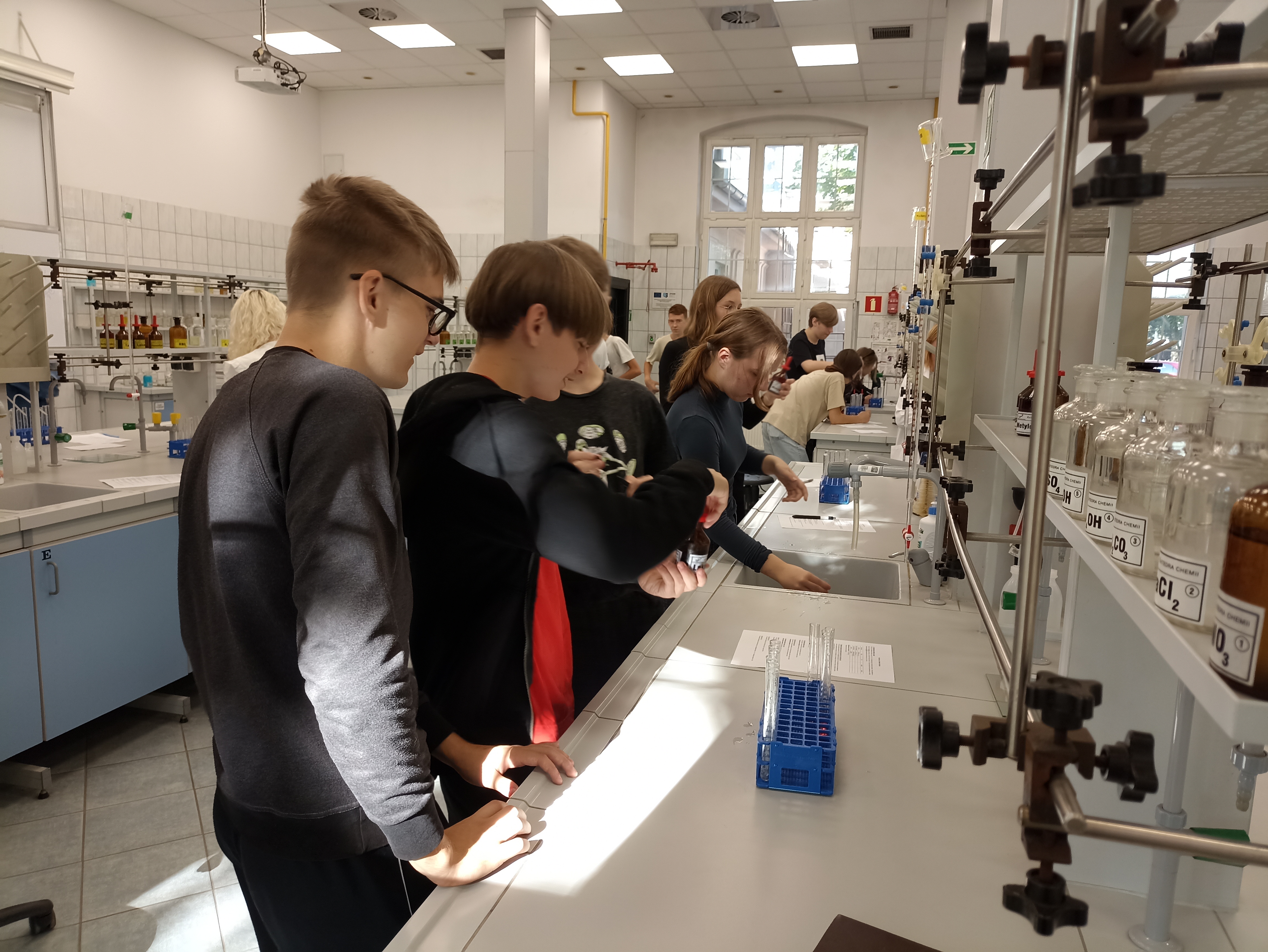 Uczniowie wykonują doświadczenia, wykorzystując do tego celu szkło, sprzęt laboratoryjny oraz odczynniki. 